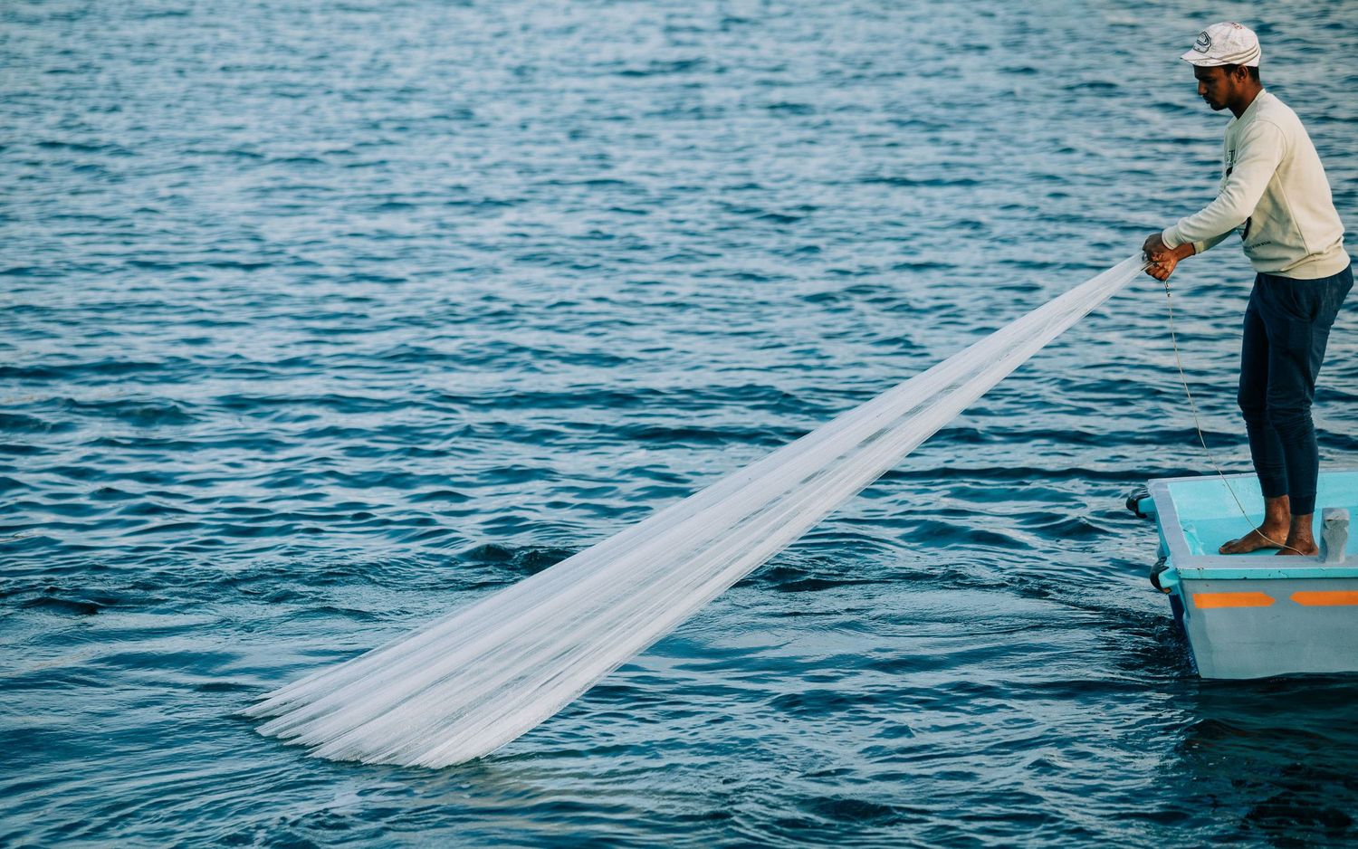 Long white fishing nets being cast into bright blue ocean waters from small boats.