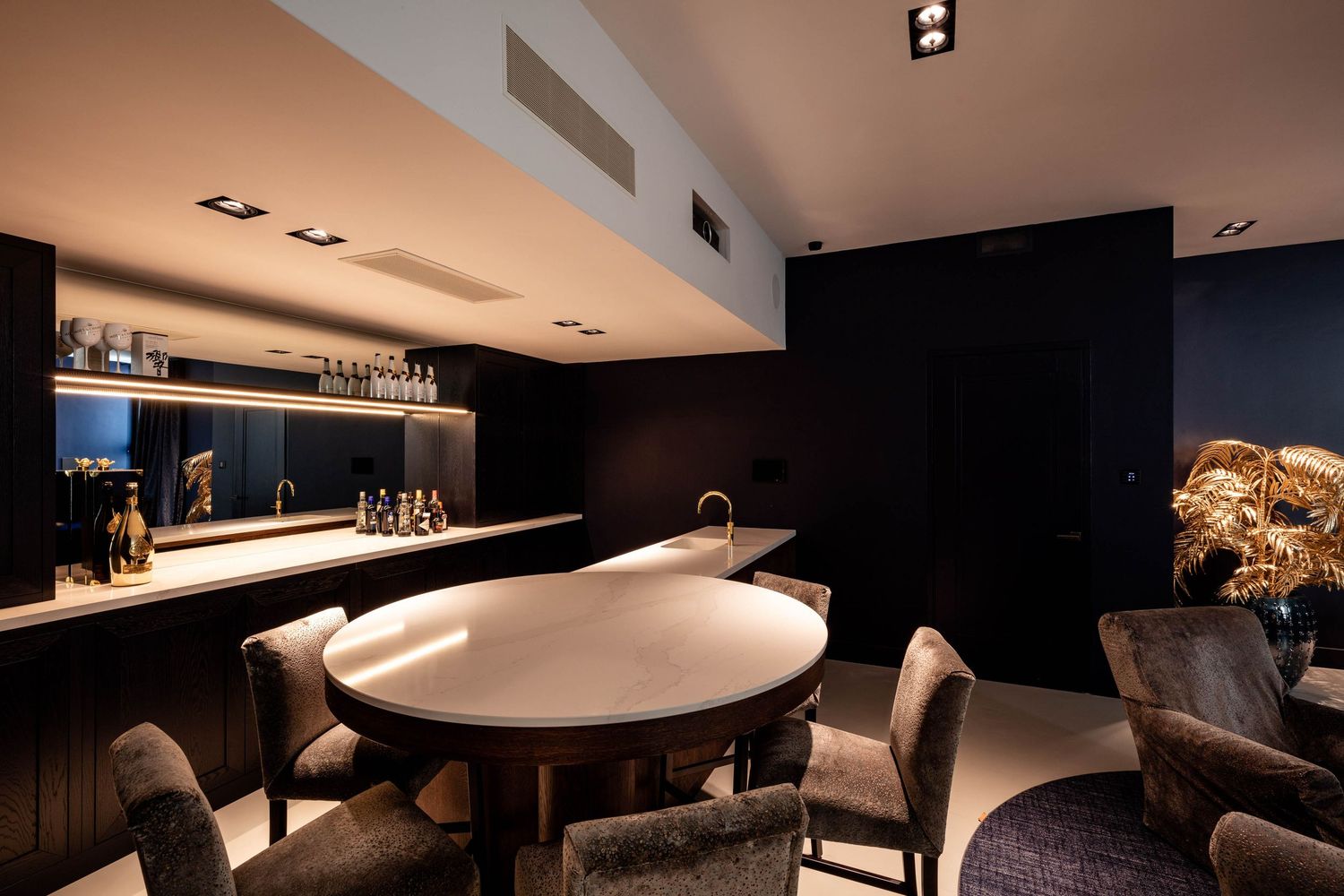 Modern luxury bar interior with curved white counter, leather seating and dramatic mood lighting in dark tones.