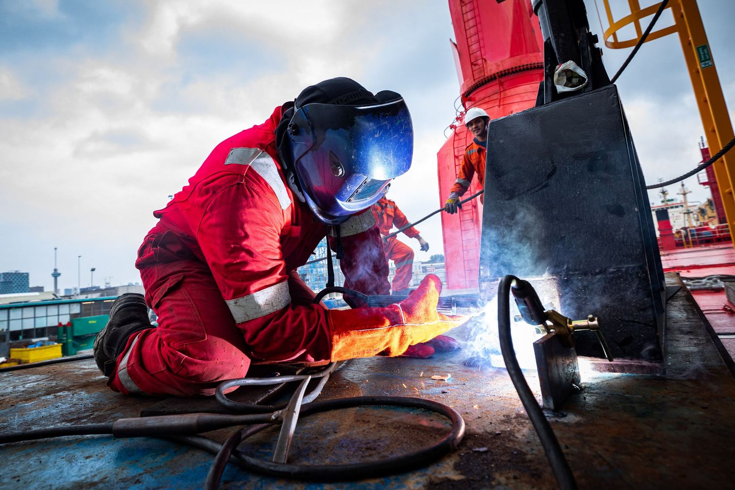 Workers performing welding operations on industrial equipment with bright sparks flying.