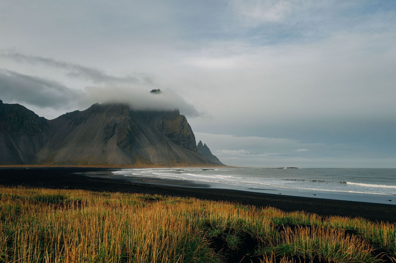 A panoramic view of rugged coastal mountains meeting the Pacific Ocean with dramatic cliffs and golden grasslands.