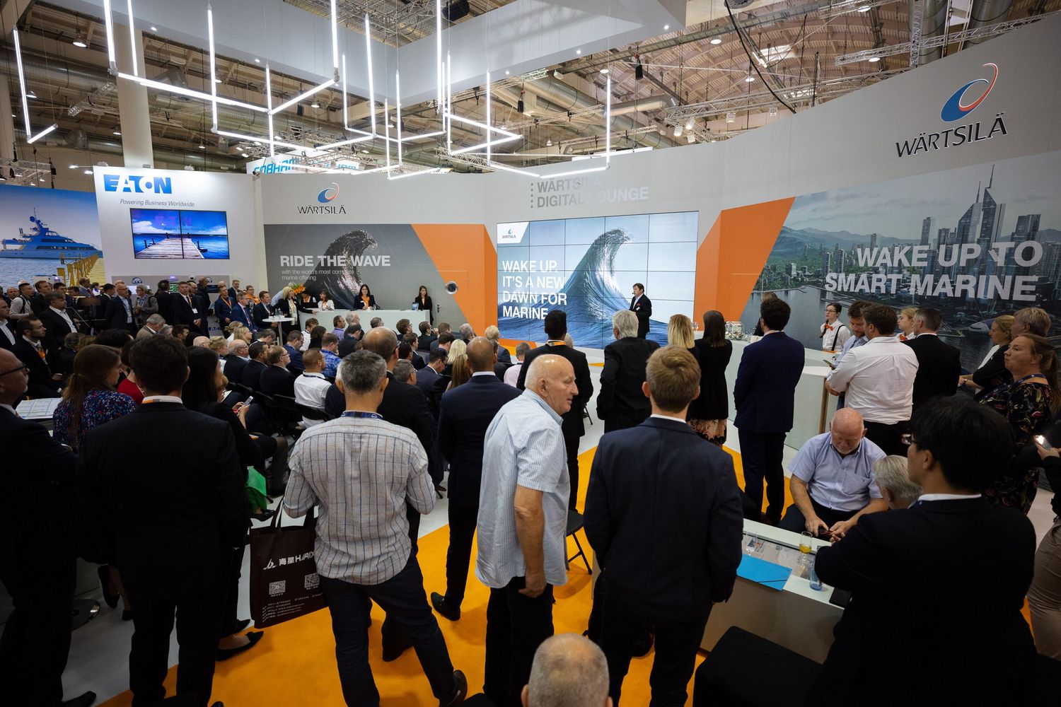 Business professionals networking and viewing displays at a large technology industry trade show exhibition floor.