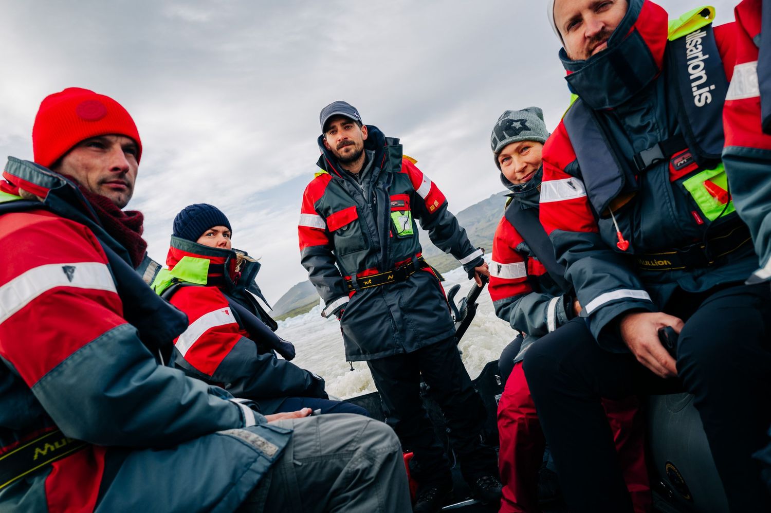 A team of emergency responders wearing red and black winter uniforms sit together during an outdoor briefing.