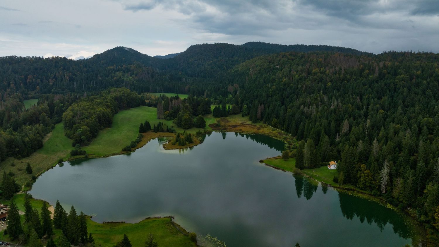 Wide panoramic view of a mountain lake surrounded by dense forest and rolling hills.