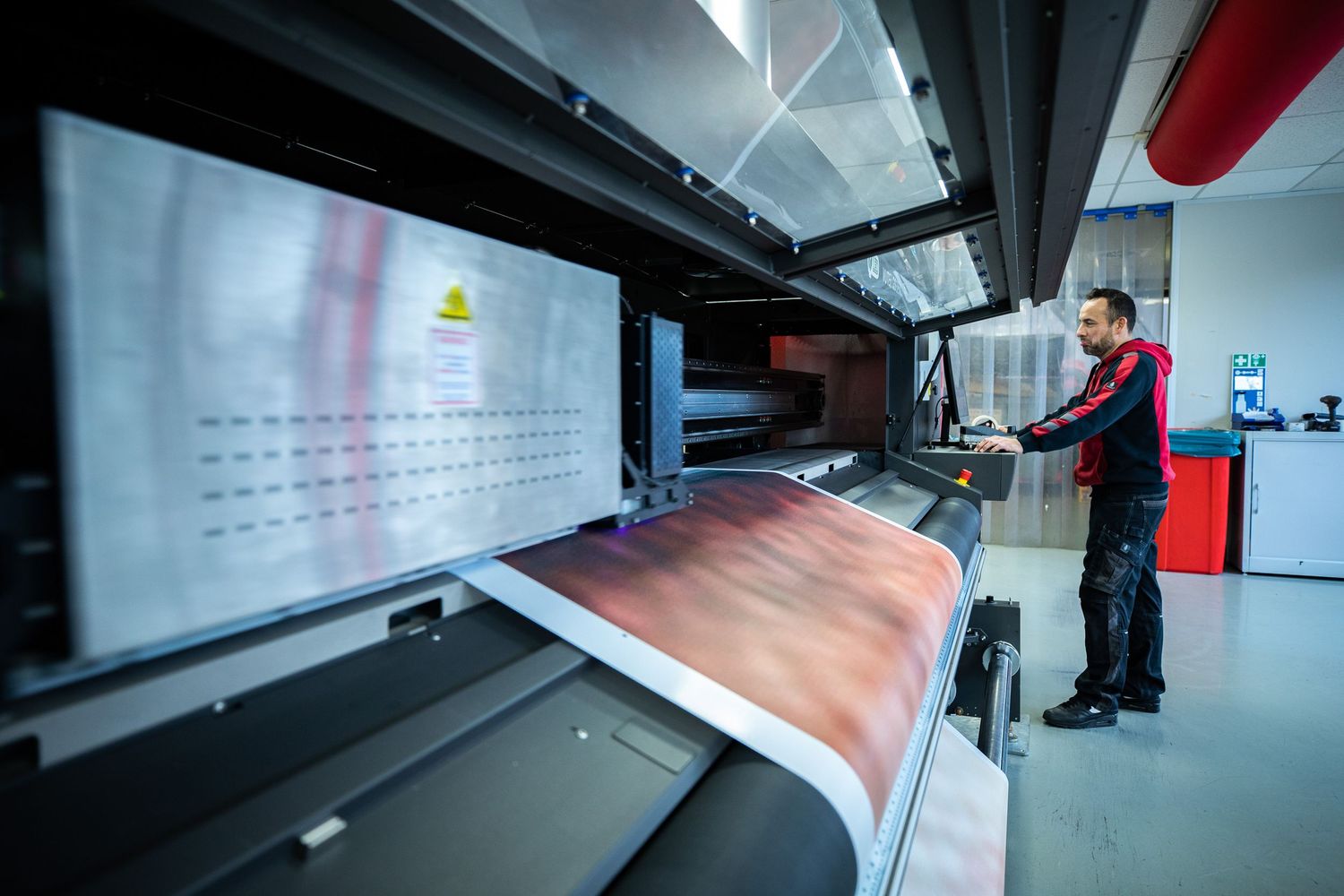Technician operating a large format industrial printing machine in a modern print facility.