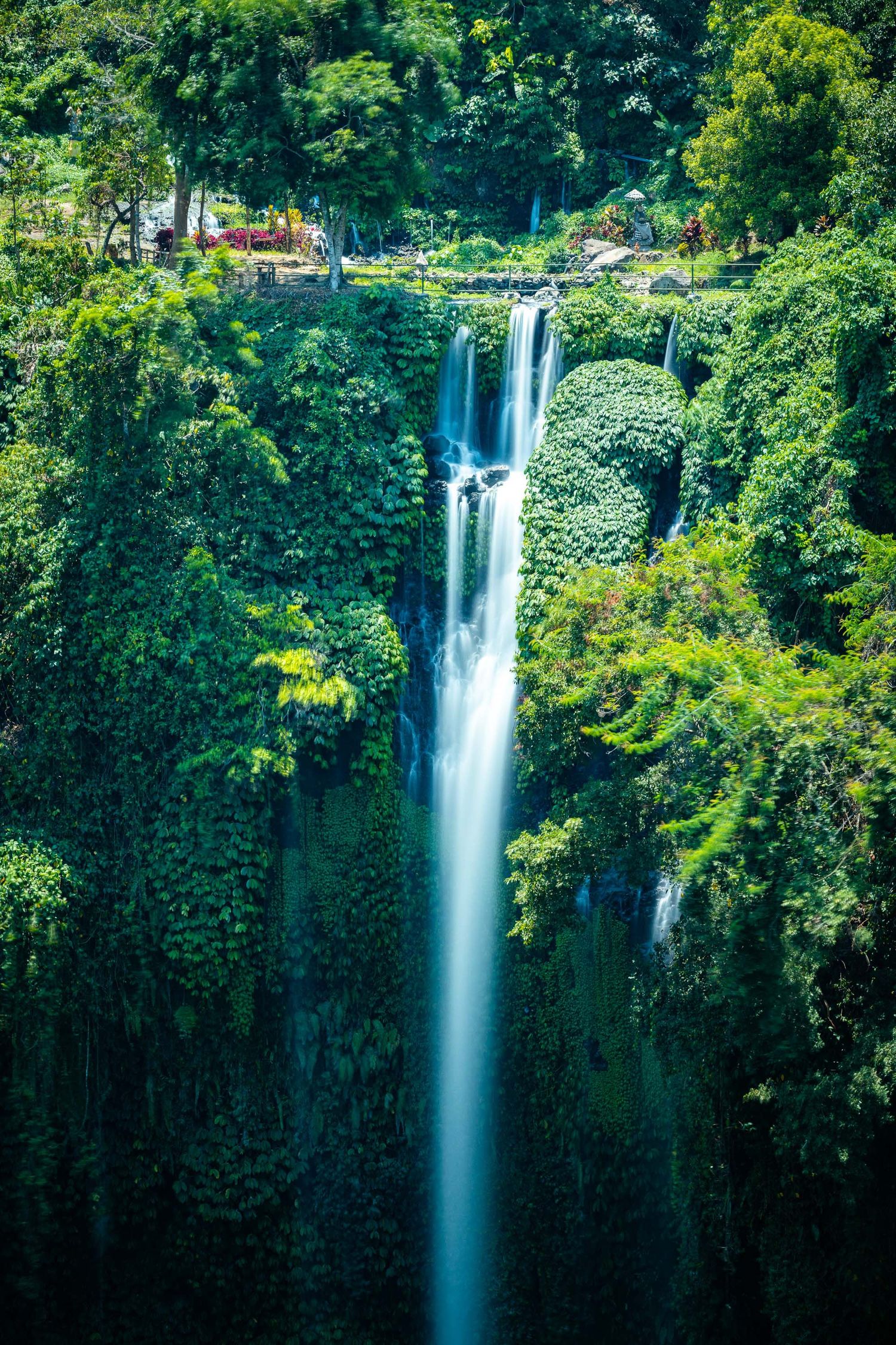 Majestic waterfall cascading down tropical cliff face surrounded by lush green vegetation.