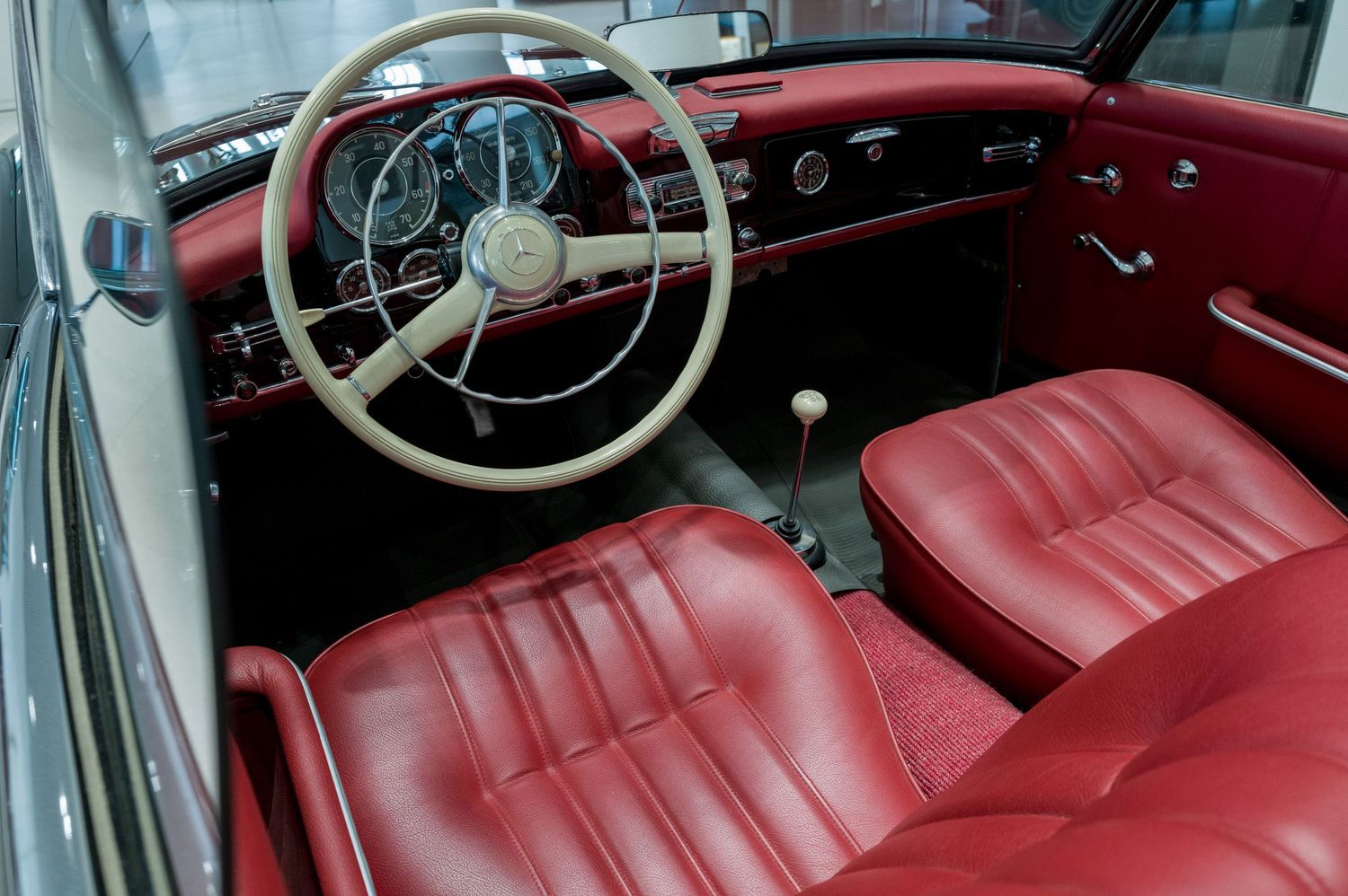 Classic Mercedes-Benz interior showing red leather seats and vintage steering wheel with chrome details.