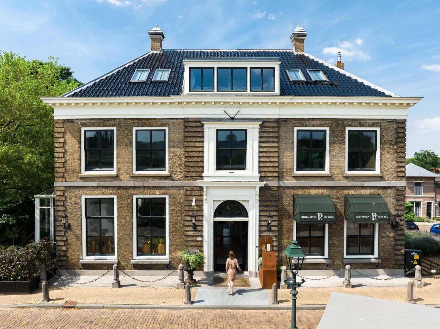 Historic Dutch brick building with symmetrical facade featuring white trim windows and central arched entrance in daytime.