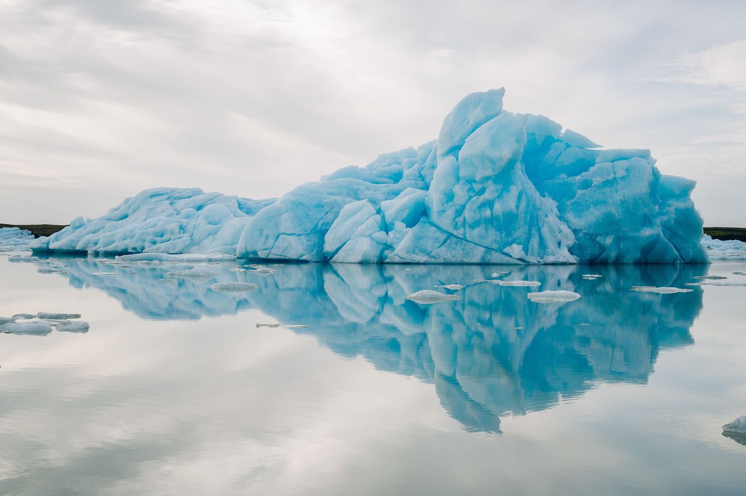 Stunning blue icebergs float serenely in glacial waters of Iceland's Jokulsarlon Glacier Lagoon under cloudy skies.