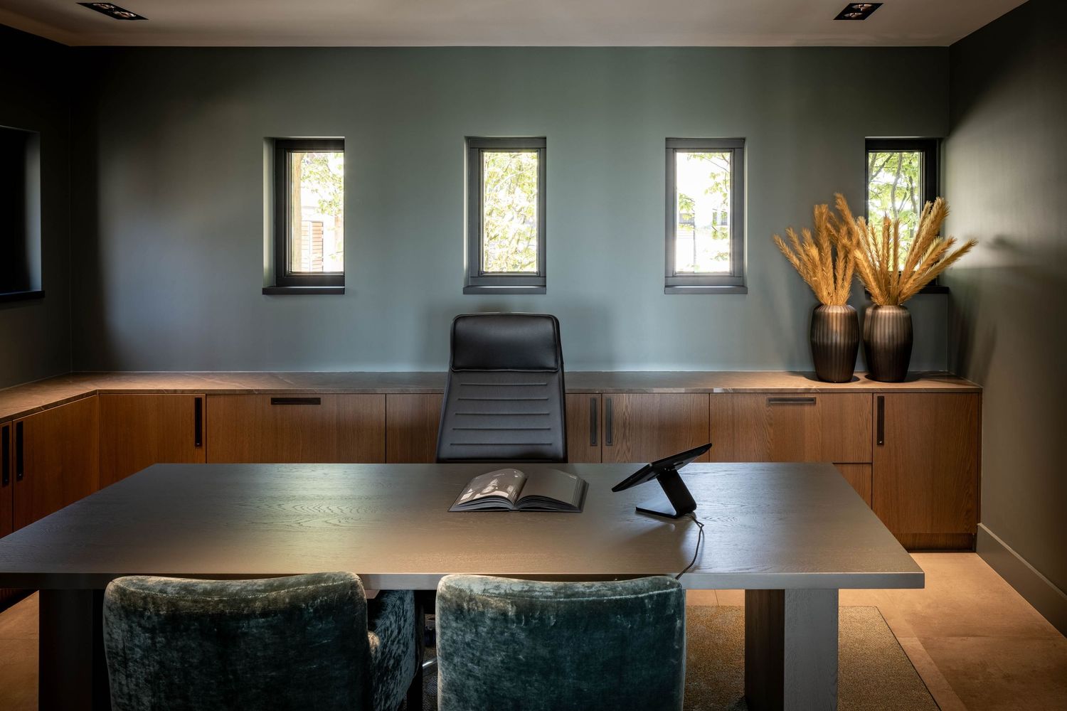 Modern office conference room with wooden walls, sleek black furniture, and natural light streaming through tall windows.