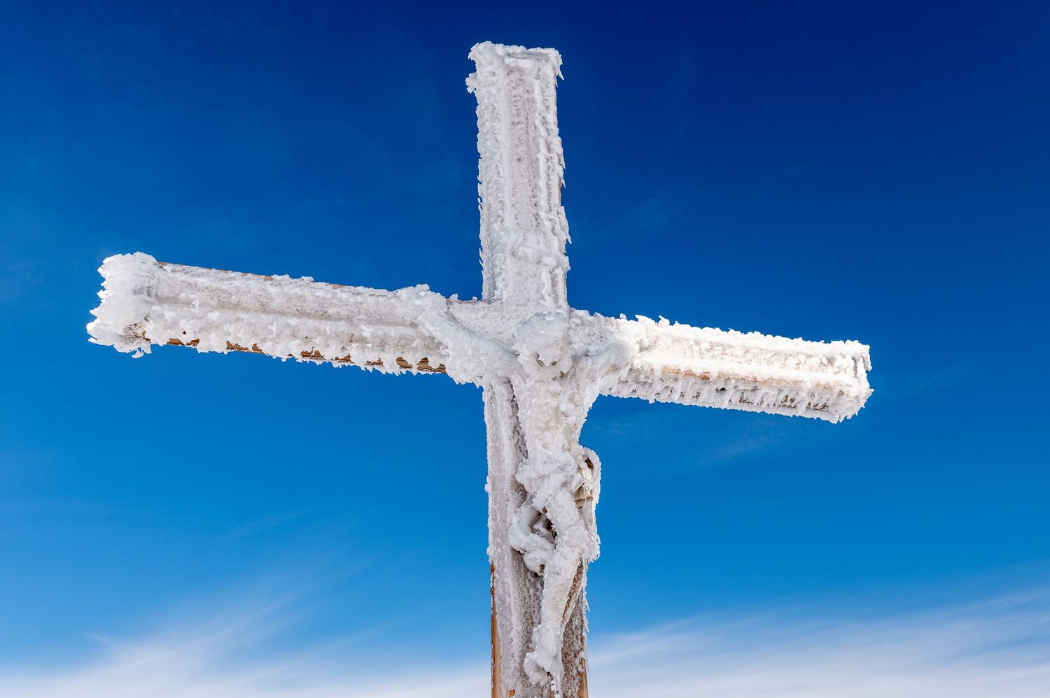 Snow-covered mountain peaks and a white cross monument against a bright blue sky.