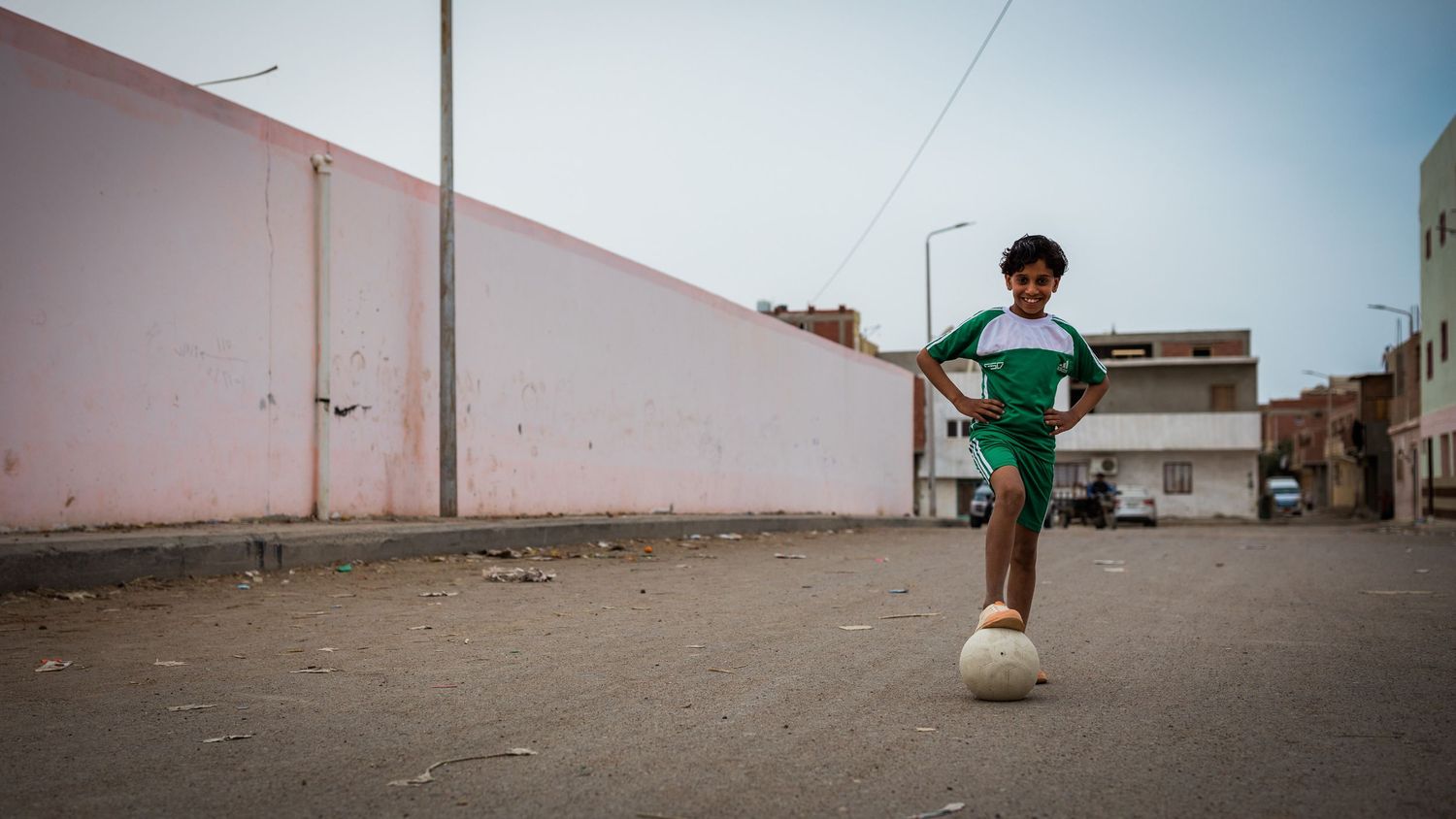 A child playing soccer alone on an empty street.