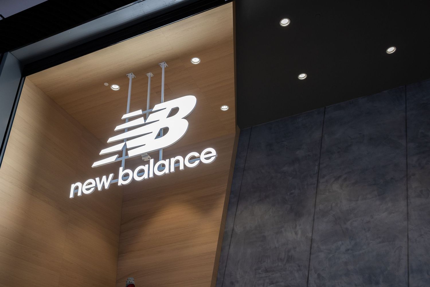New Balance store signage illuminated against dark textured wall in retail environment.