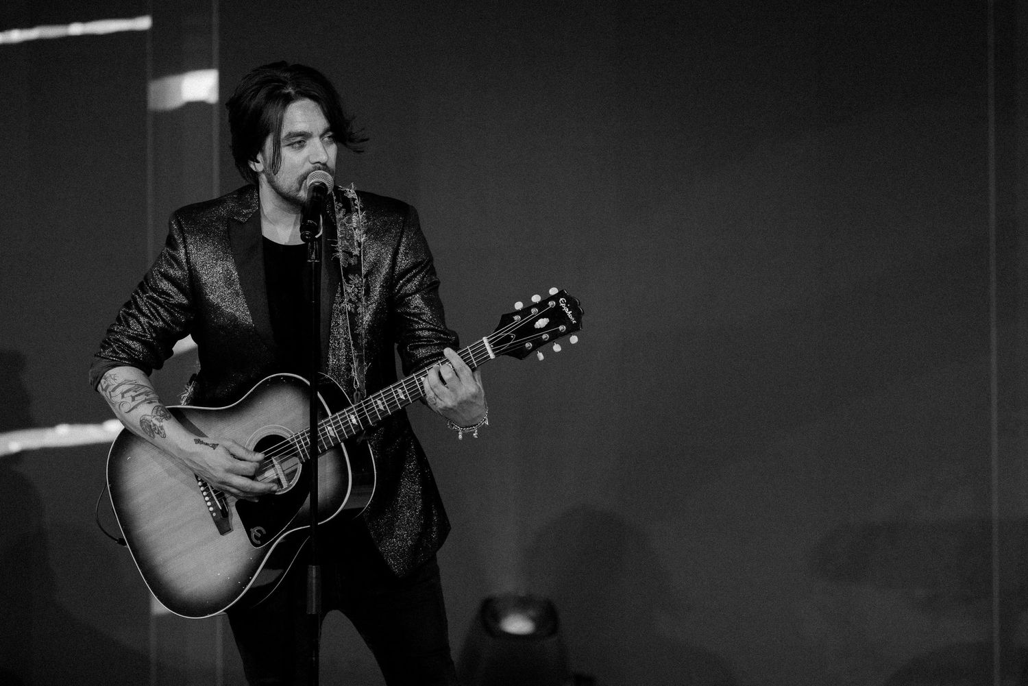 Black and white photos show a performer playing acoustic guitar on stage during a live musical performance.