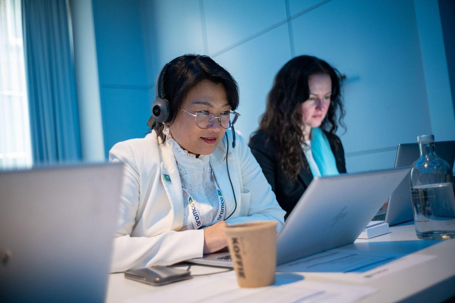 Professionals working at computer stations in a bright blue-tinted office environment.