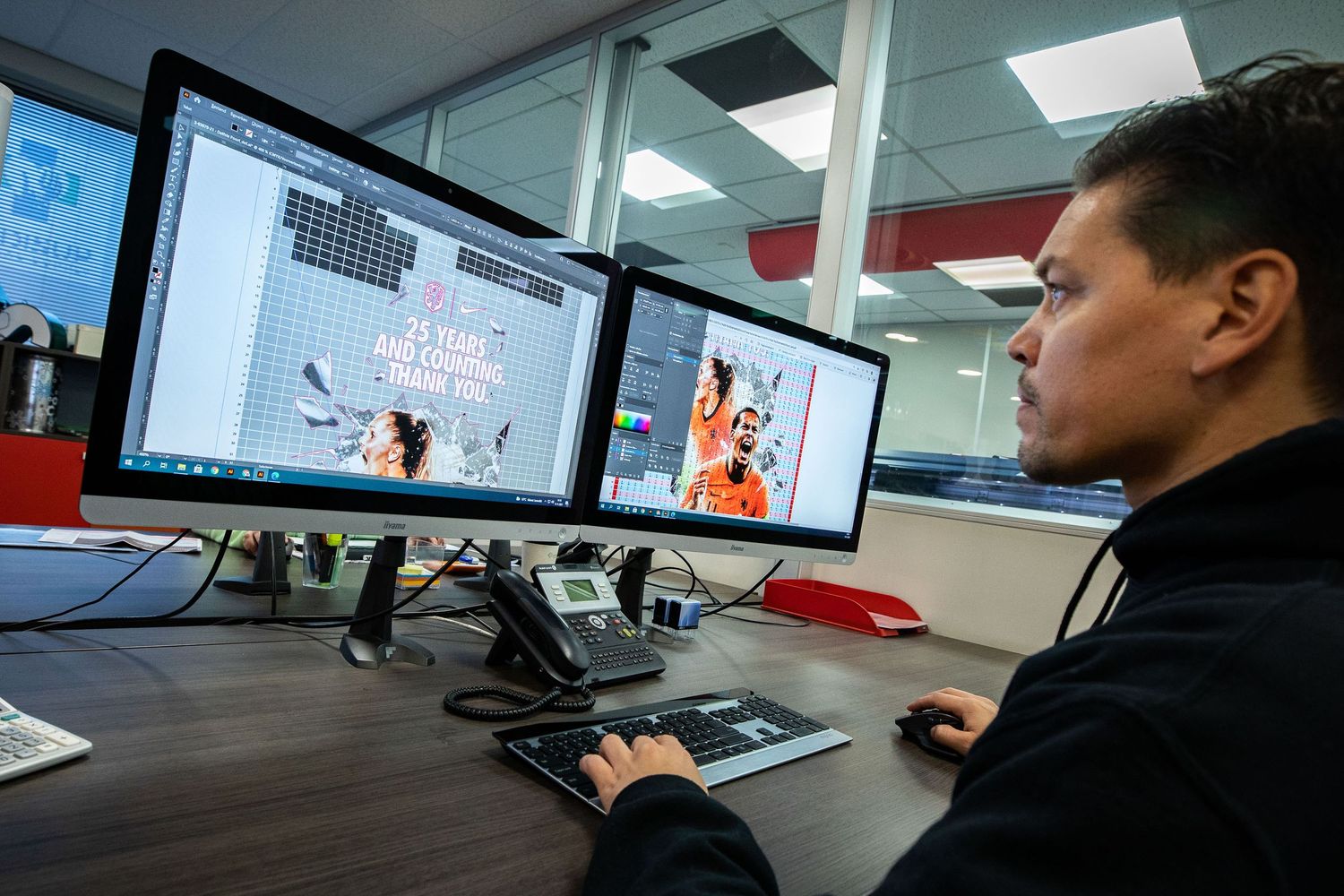 A graphic designer works at a dual monitor workstation editing vibrant digital artwork in a modern office.
