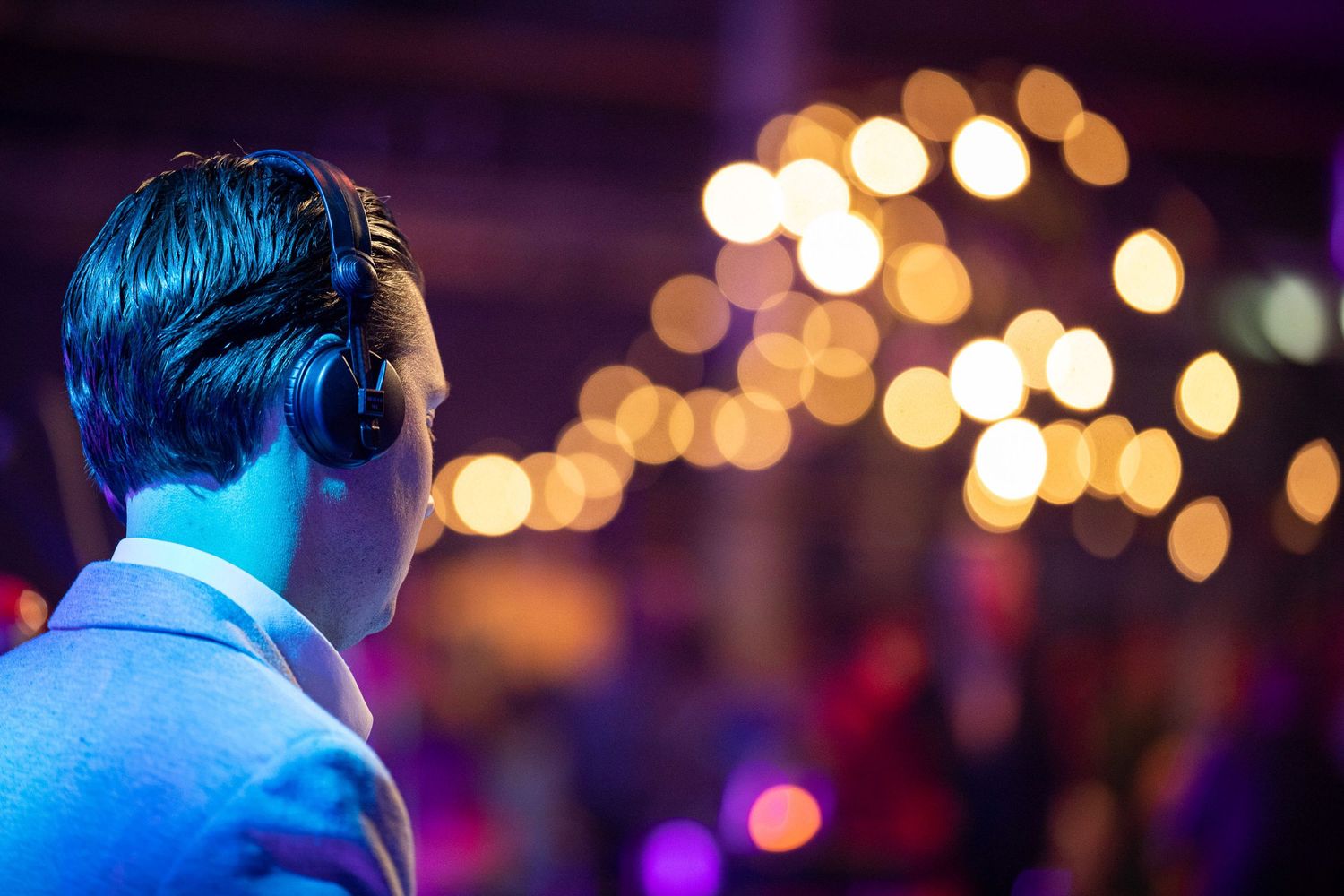 A DJ performs at a nightclub with colorful blue lighting and bokeh effects in the background.