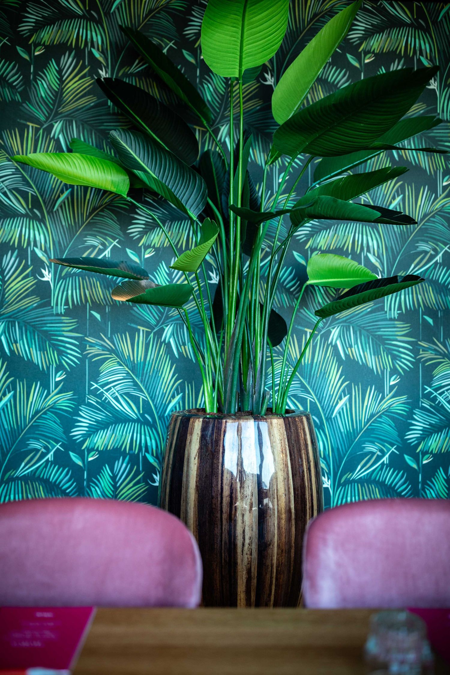 Tropical palm leaf wallpaper creates a vibrant backdrop behind pink seating in a modern restaurant interior.