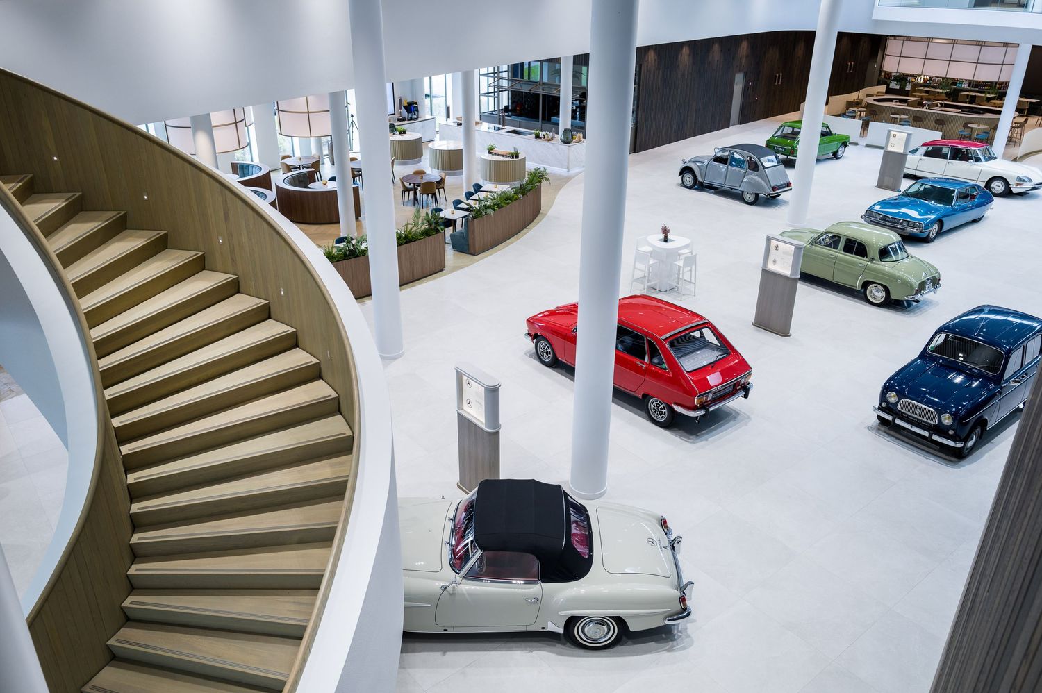 Classic vintage cars on display in a modern showroom with curved white spiral staircases and bright lighting.