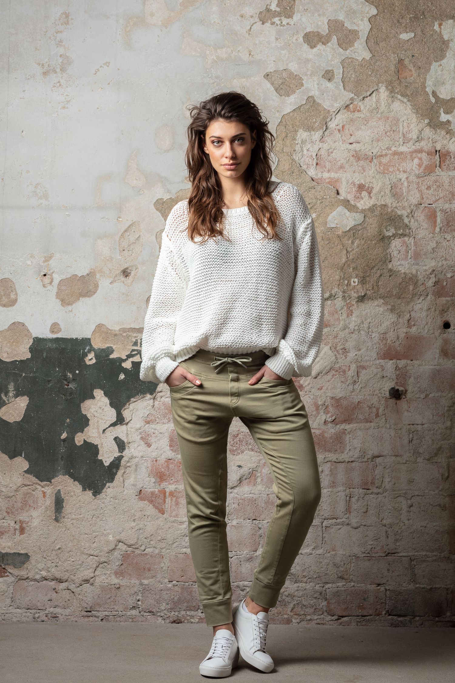 Lifestyle fashion photos showing white knit sweater and olive pants against textured wall backdrop.