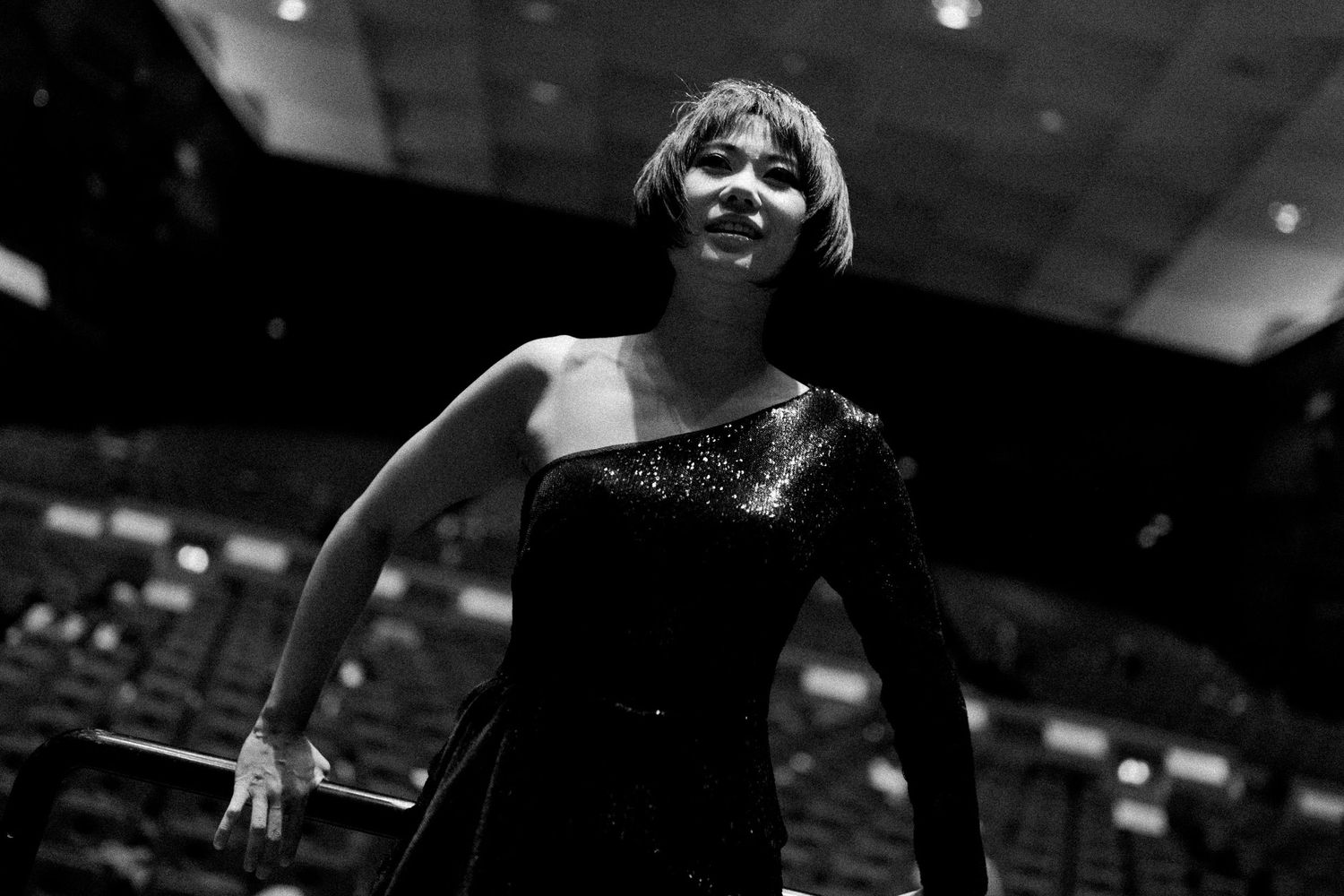 A dramatic black and white shot of a performer in a sequined dress with expressive movement on stage.