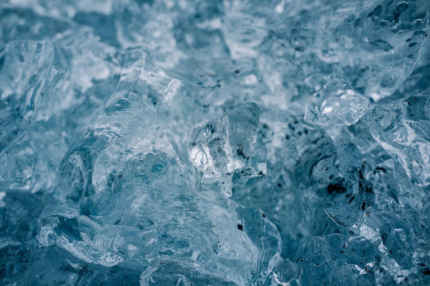 Close-up macro photograph of translucent blue ice crystals showing intricate frozen patterns and textures.
