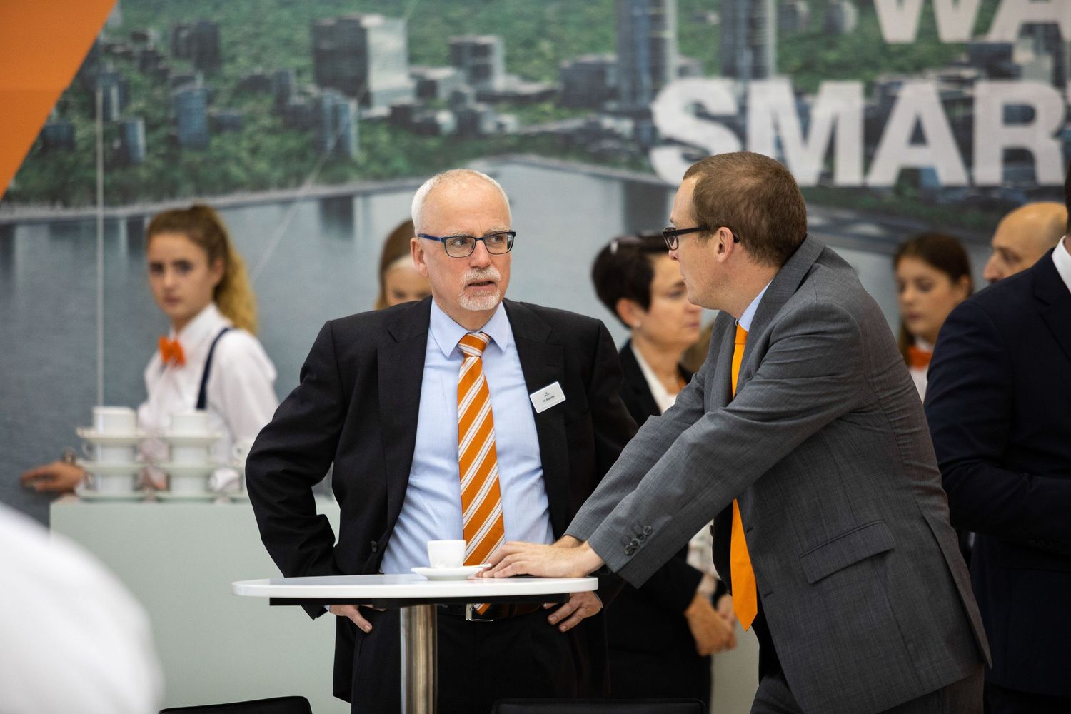 Two business professionals in suits having a discussion at a table during a corporate event.