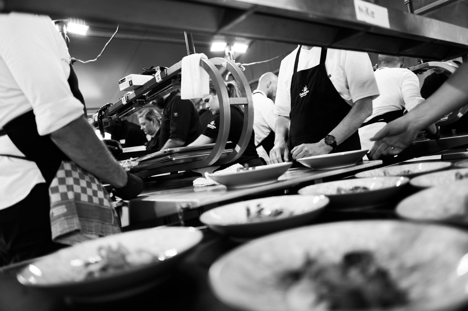 Close-up black and white shot of hands preparing food in a restaurant kitchen.