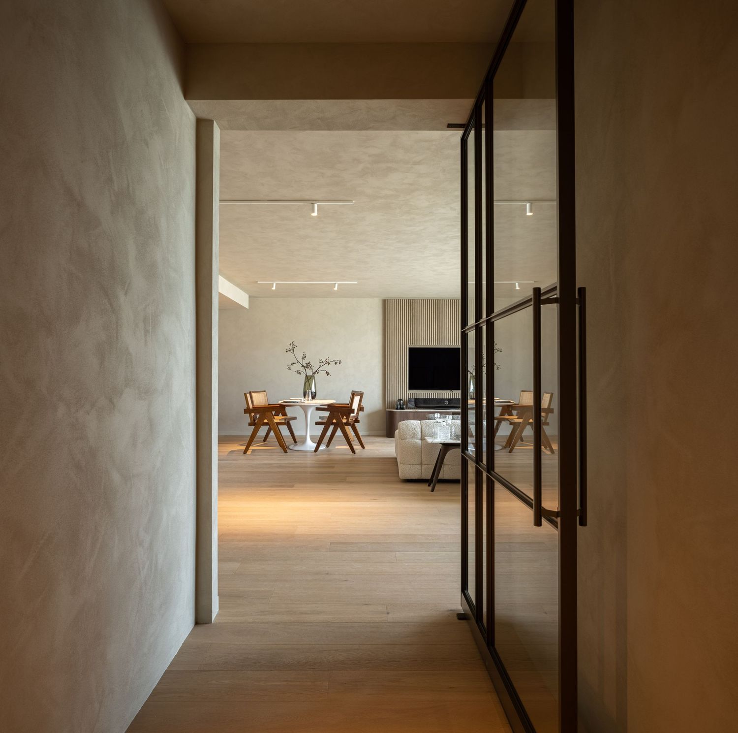 Minimalist interior hallway with concrete walls and black metal frames leading to a bright open space at the end.