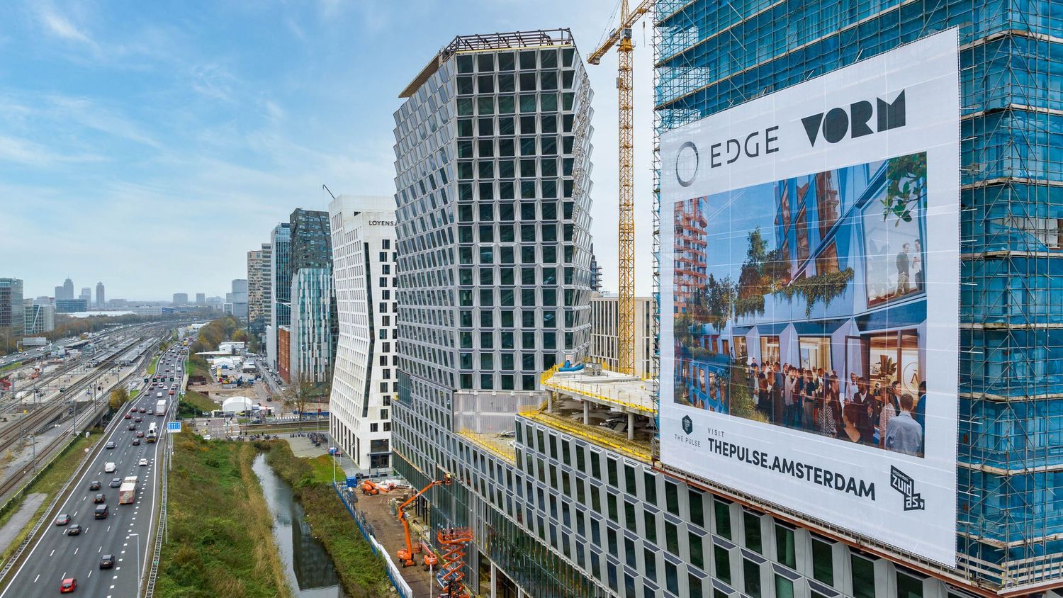 Aerial view of EDGE and VORM skyscrapers under construction in Amsterdam, with highway and city skyline visible.