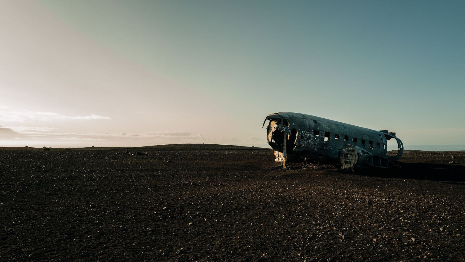A panoramic view of a desolate desert landscape with a lone vehicle silhouetted against the horizon at sunset.