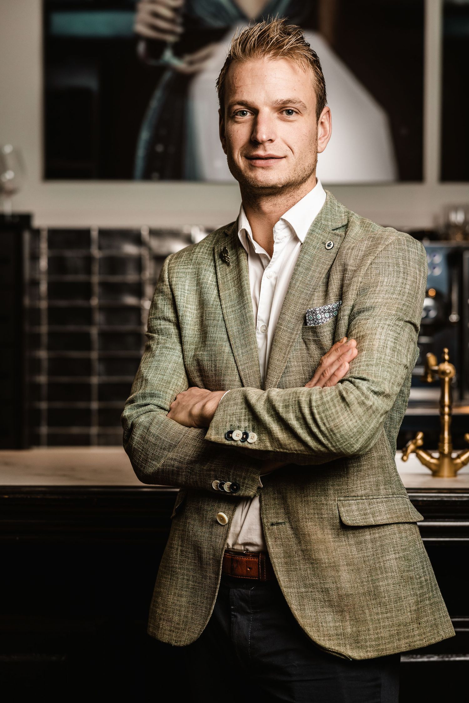 Professional in a textured gray blazer and white shirt stands confidently with arms crossed in an upscale bar setting.
