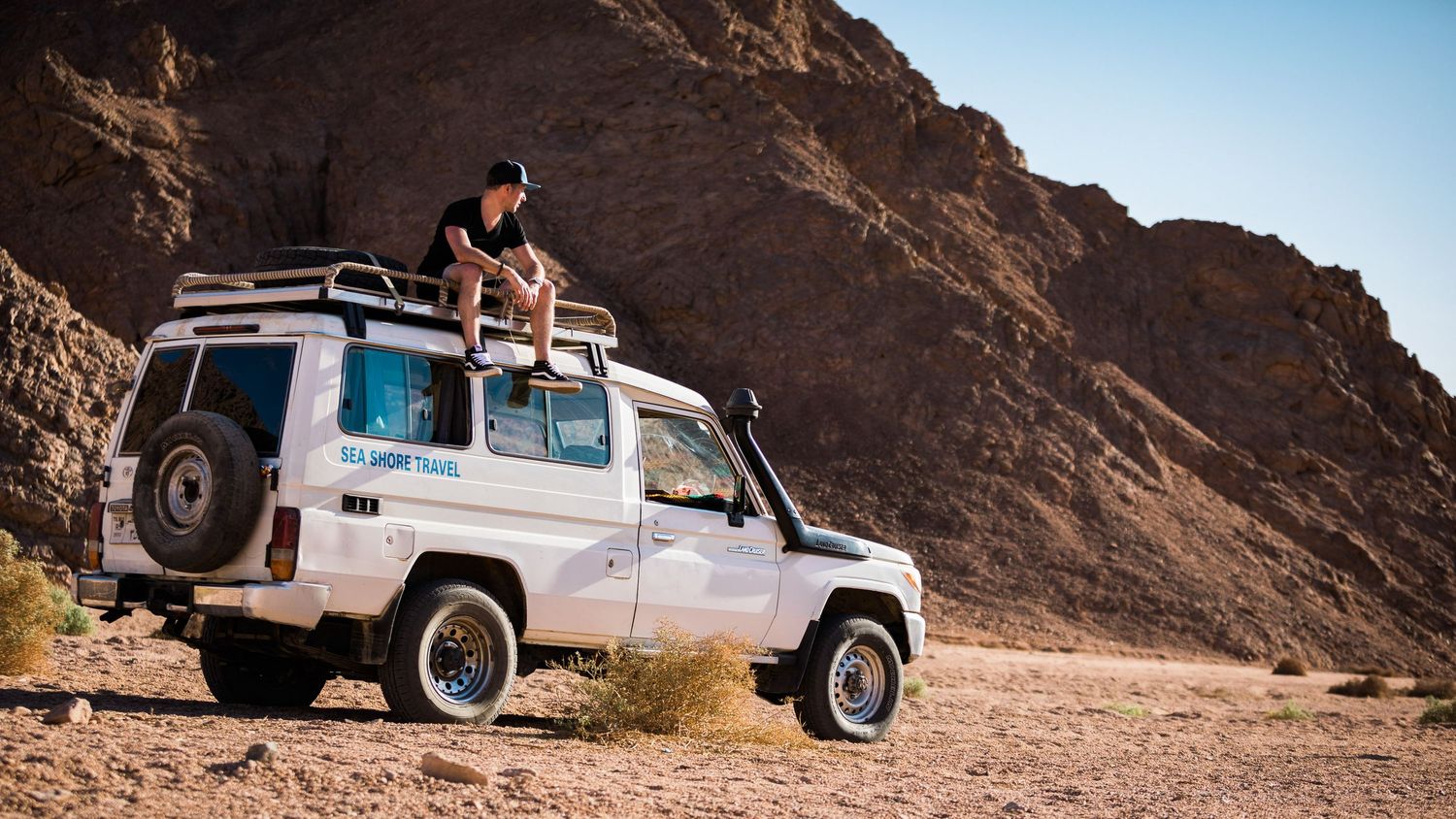 Person sitting on top of a white Land Cruiser 4WD in a rocky desert canyon landscape.