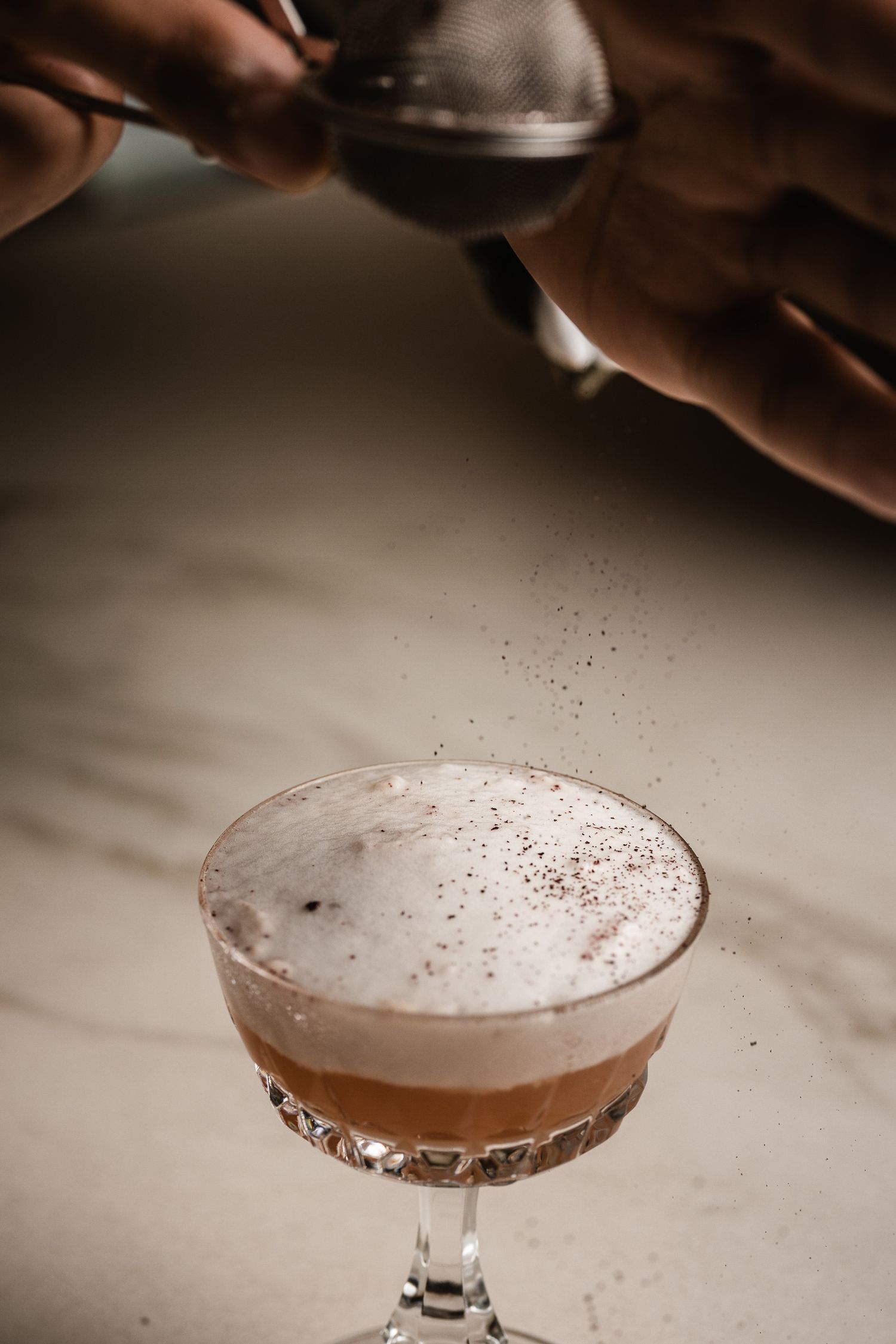 A series of cocktail making steps showing a frothy pink drink being poured and garnished in a coupe glass.