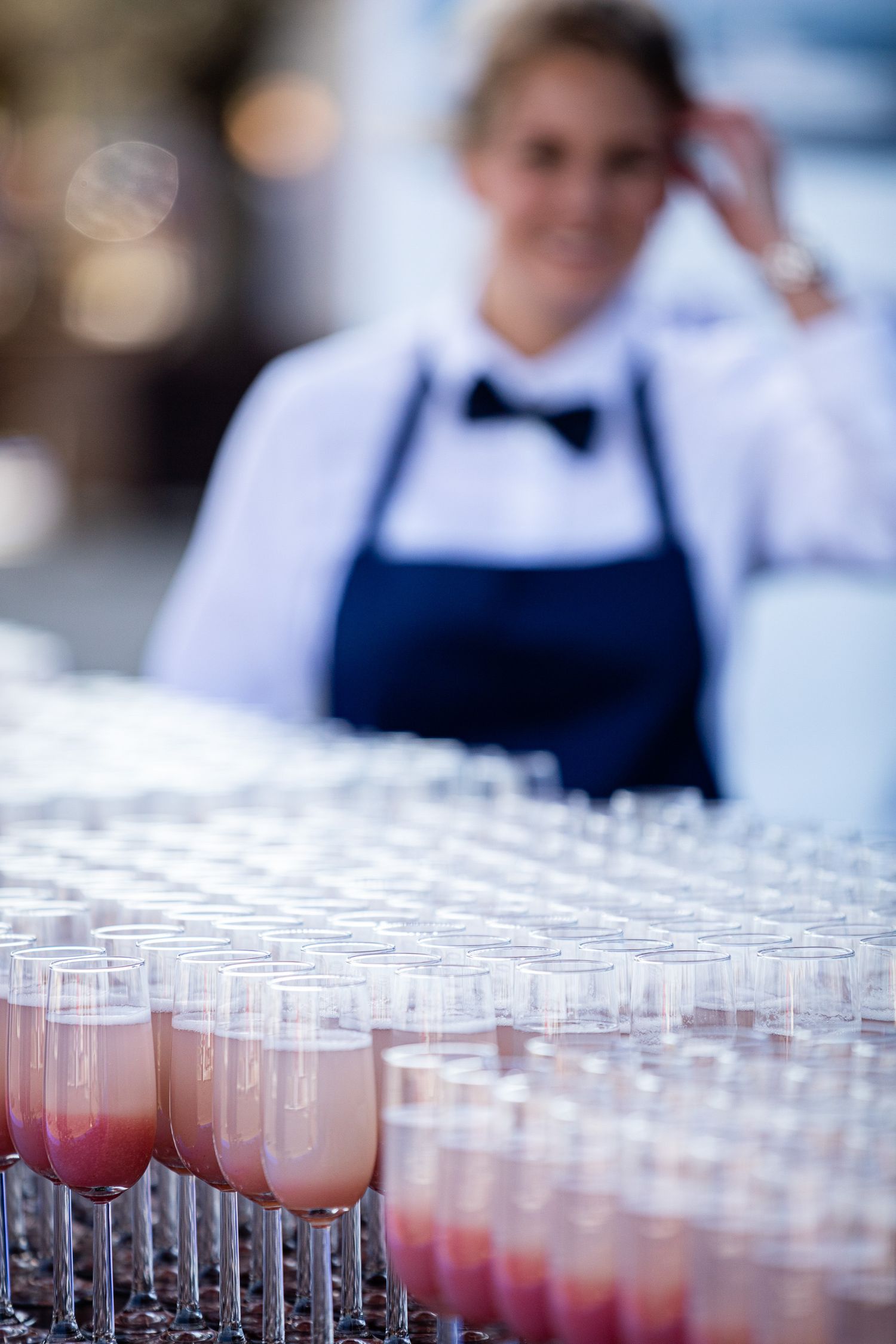 Rows of pink cocktails in clear glasses arranged on trays at an upscale catering event.