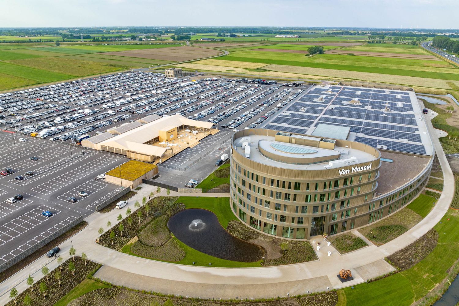 Modern circular office building with large parking lot and solar panels viewed from aerial perspective.