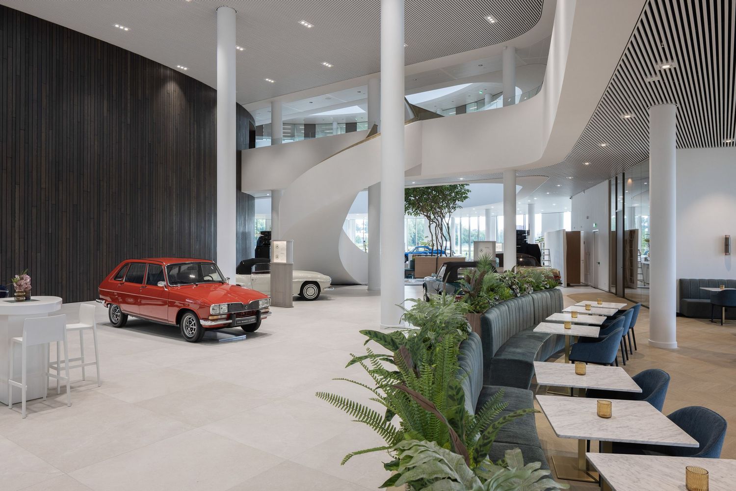 Modern office lobby interior with vintage red car display, white columns, and contemporary seating areas with indoor plants.