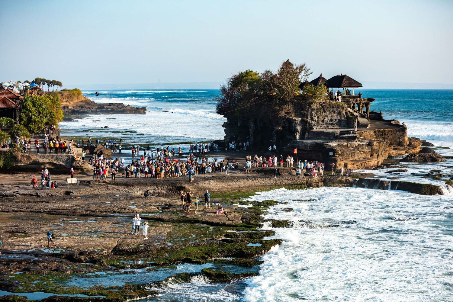 Rocky coastal landscape with Tanah Lot temple silhouette and crashing waves.