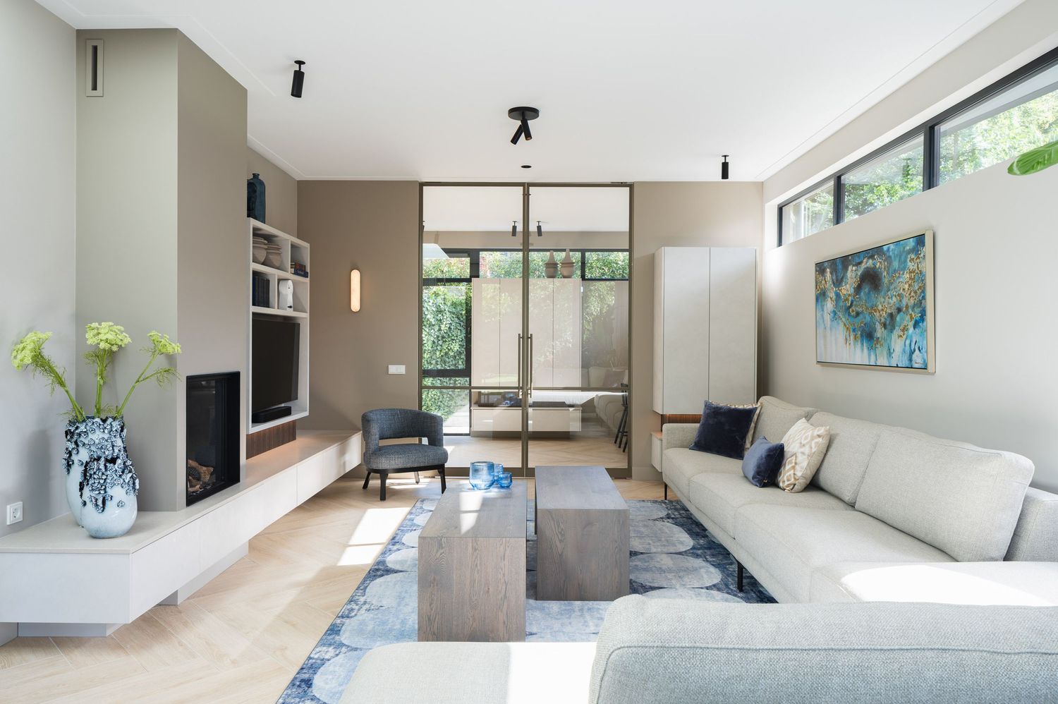 Modern living room with sectional sofa, blue rug, and large windows showcasing a minimalist contemporary design style.