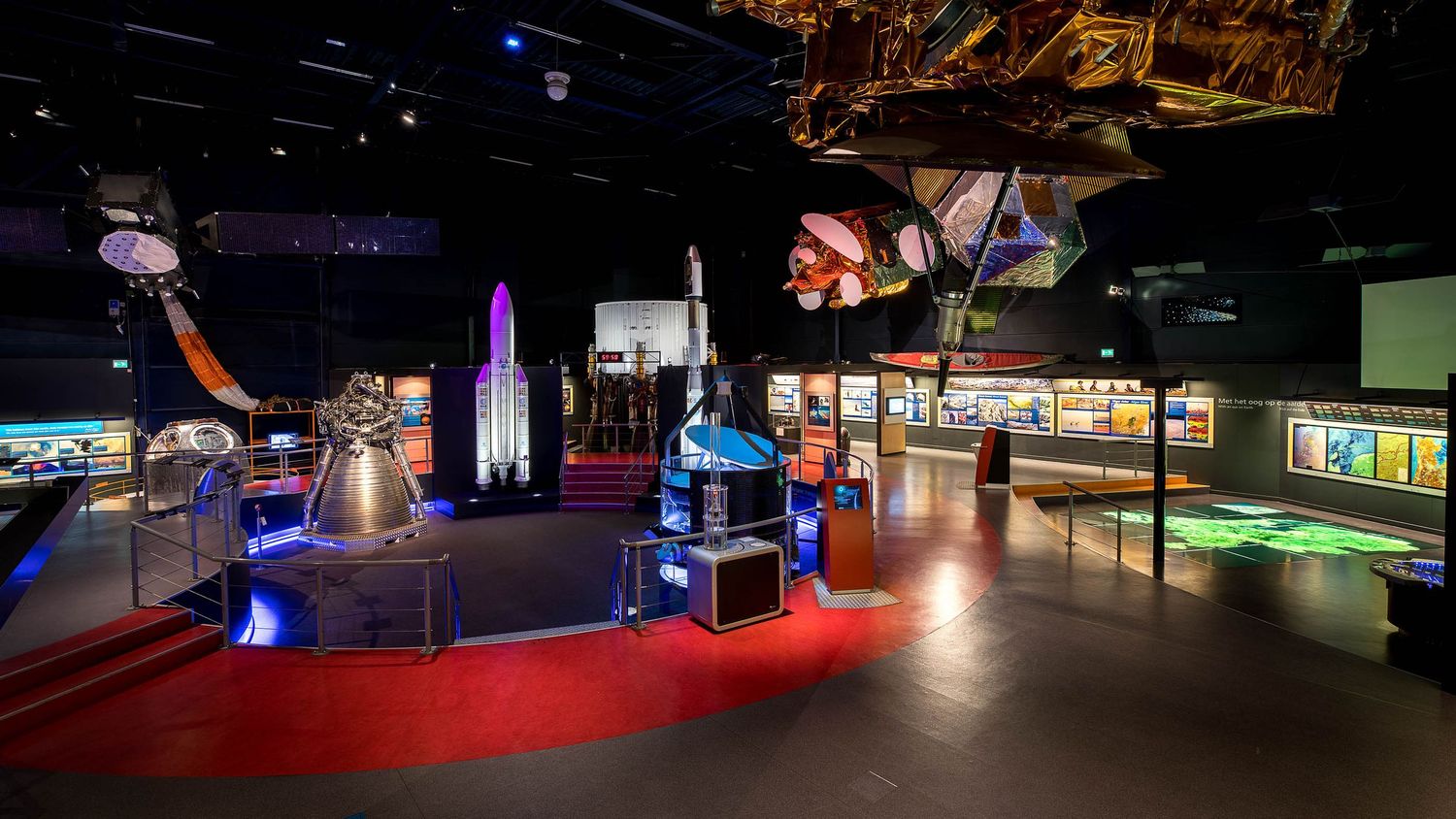 Space museum exhibit showcasing rocket models, satellites, and interactive displays under dramatic colorful lighting.