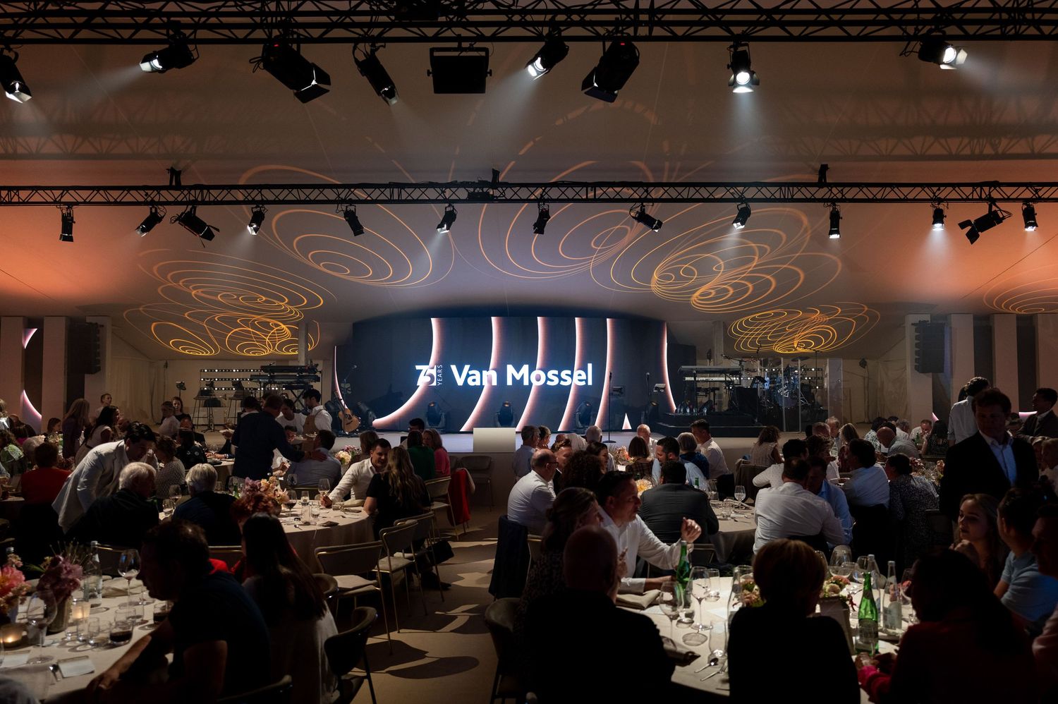 A dimly lit banquet hall with tables and chairs arranged for a formal event and spotlights illuminating the space.