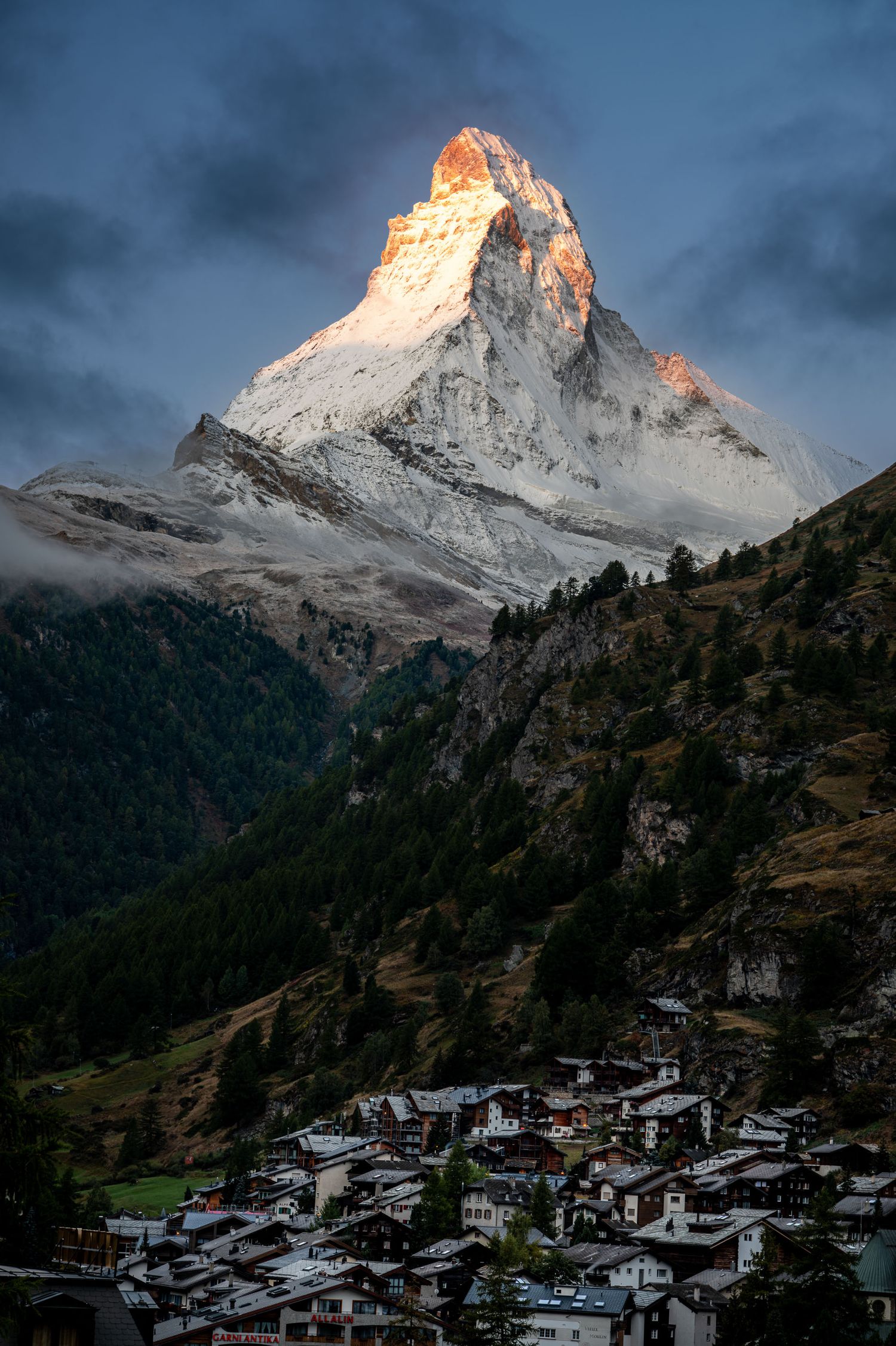 Alpine village nestled beneath majestic Matterhorn peak during golden sunrise.