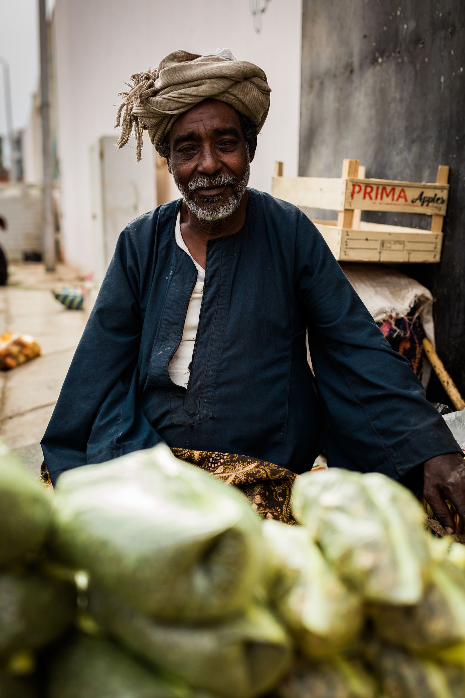 A vendor in traditional dress selling fresh produce at a local market stall.