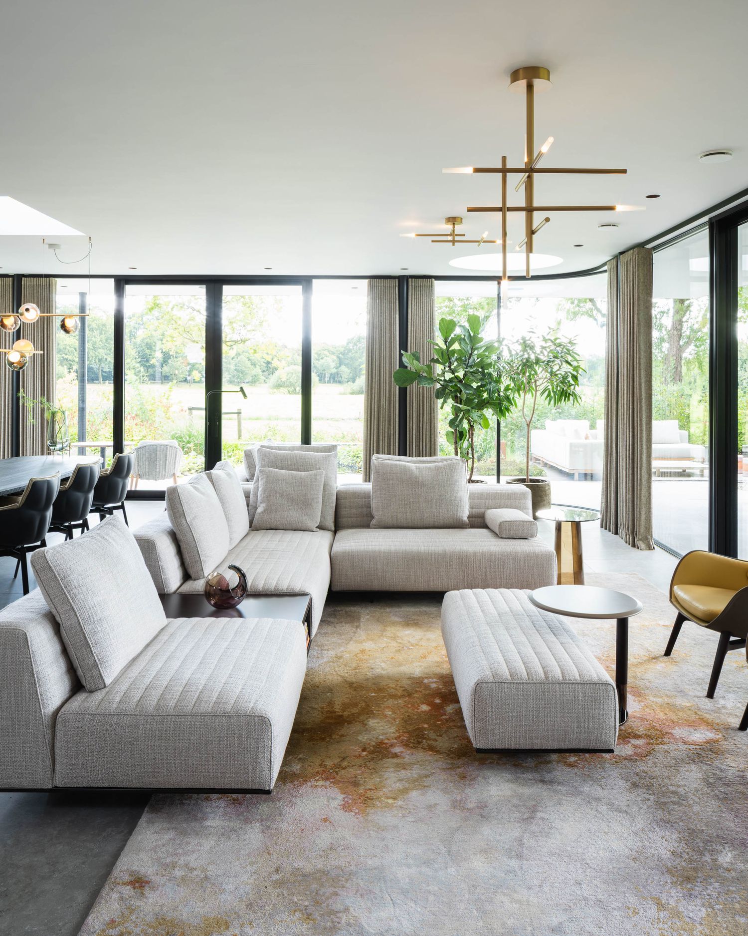 Modern living room features a plush grey sectional sofa with floor-to-ceiling windows and abstract patterned carpet.