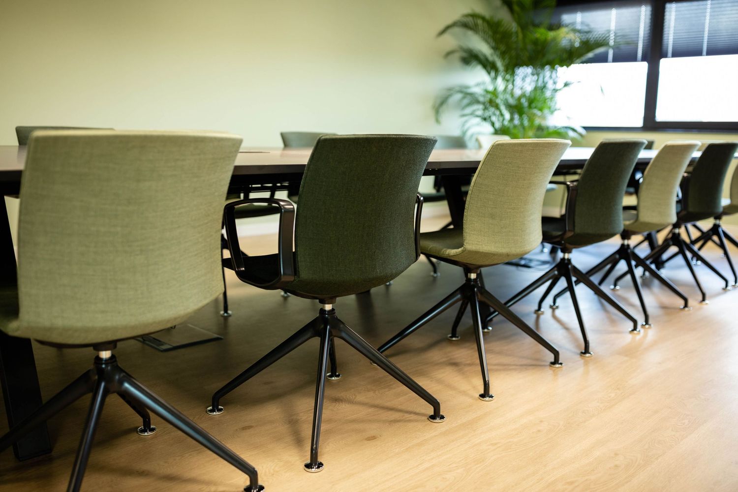 Modern office chairs with green upholstery and black metal bases arranged in a row along a wooden floor.