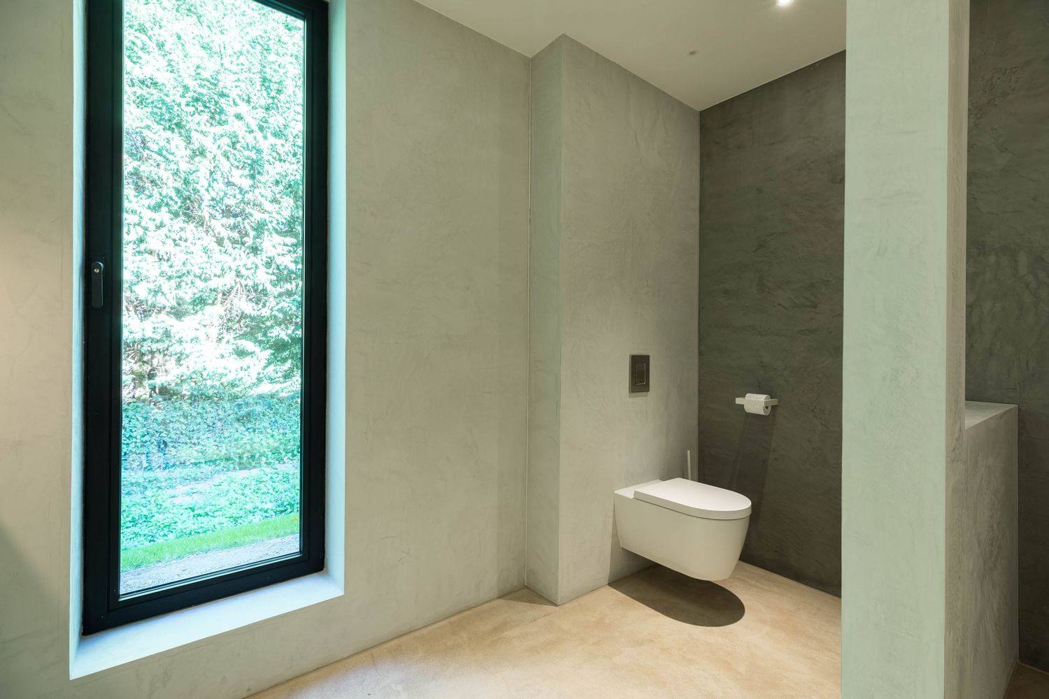 Modern bathroom interior with wall-mounted toilet, large window, and contrasting gray accent wall against white walls.