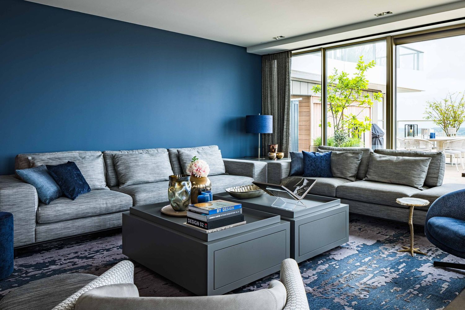 Modern living room interior with blue carpet, gray sofa, and large windows offering natural light and city views.