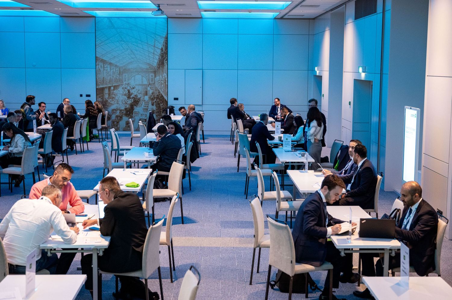 Modern office space with multiple workstations and people having business discussions.
