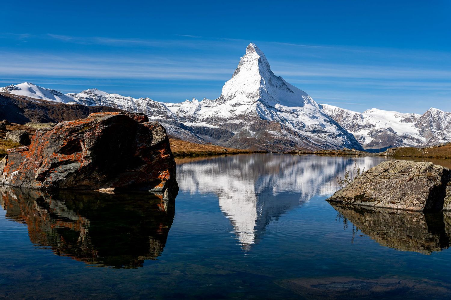 Perfect reflection of Matterhorn peak in crystal clear alpine lake under blue skies.