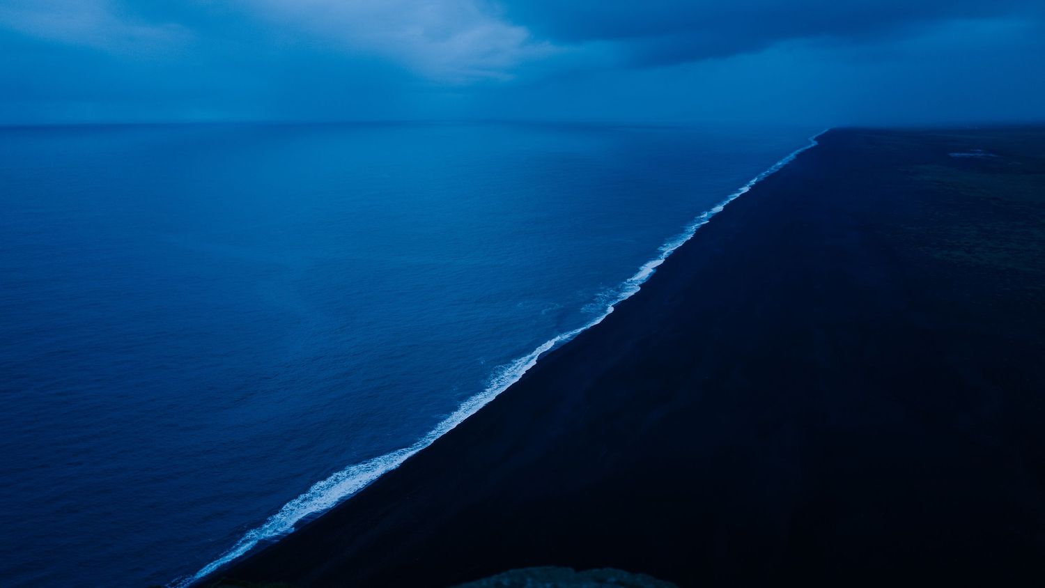Aerial view of a dramatic coastline where dark mountains meet turquoise ocean waters under a blue sky.