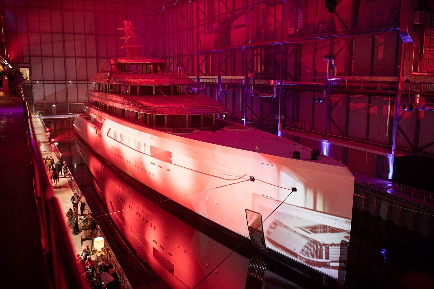 Red neon lights illuminate a long corridor with reflective tiled walls and floor creating a futuristic atmosphere.